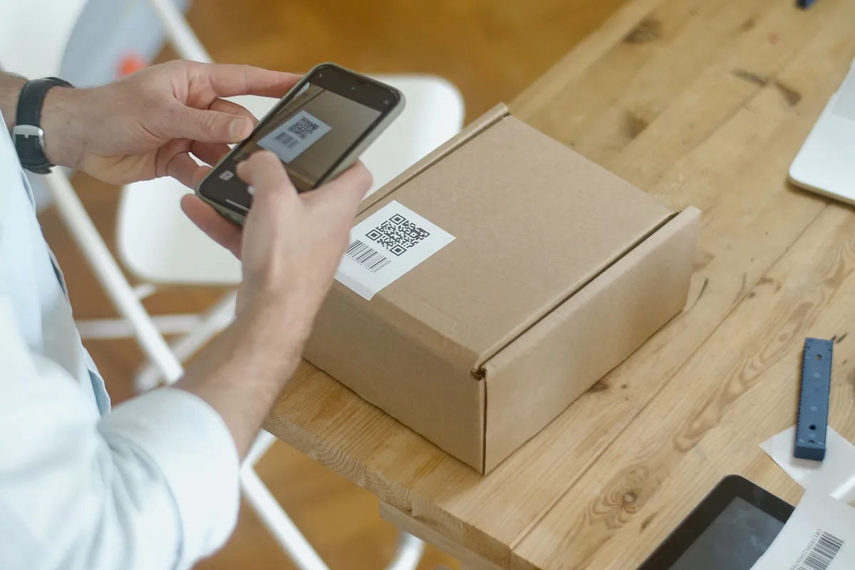 Hands scanning the QR code label on a cardboard box with a smartphone